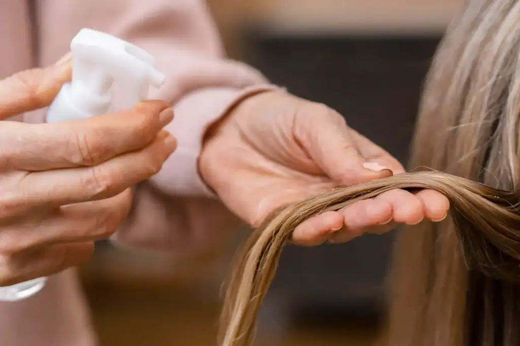 Stylist applying wig detangler spray to blonde wig in Minnesota salon.
