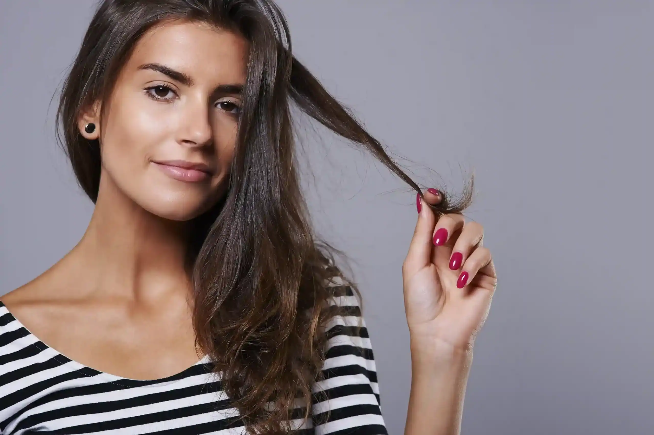 Woman with long brown hair holding a strand, showcasing wigs in Minnesota.